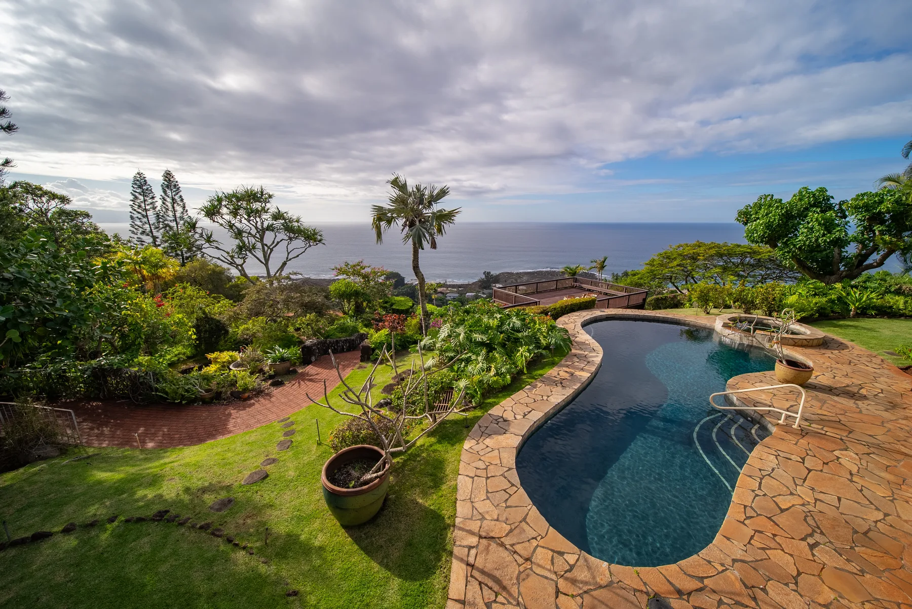 A curved swimming pool sits in a landscaped garden overlooking the ocean.