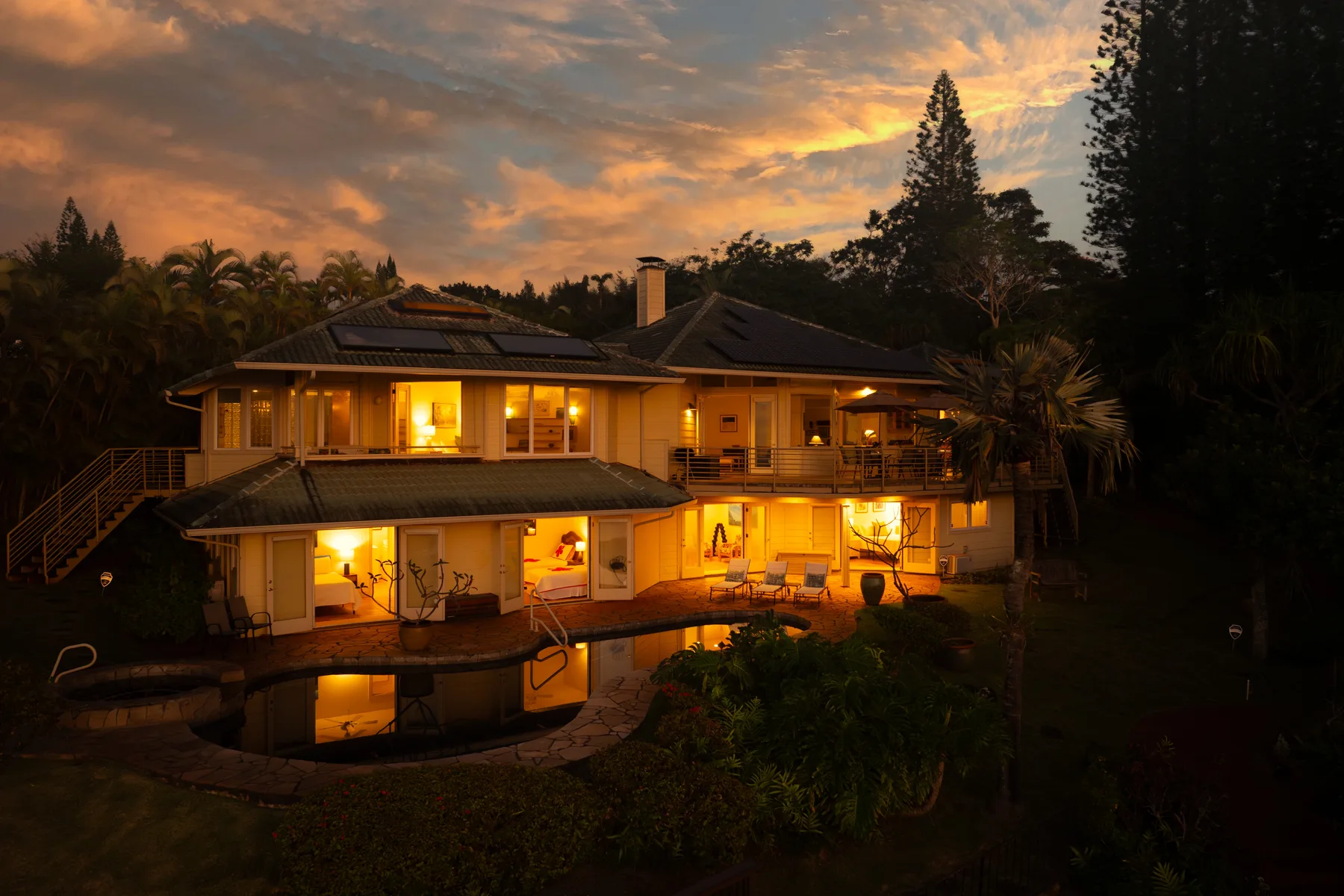 A large illuminated house beside a swimming pool at sunset.
