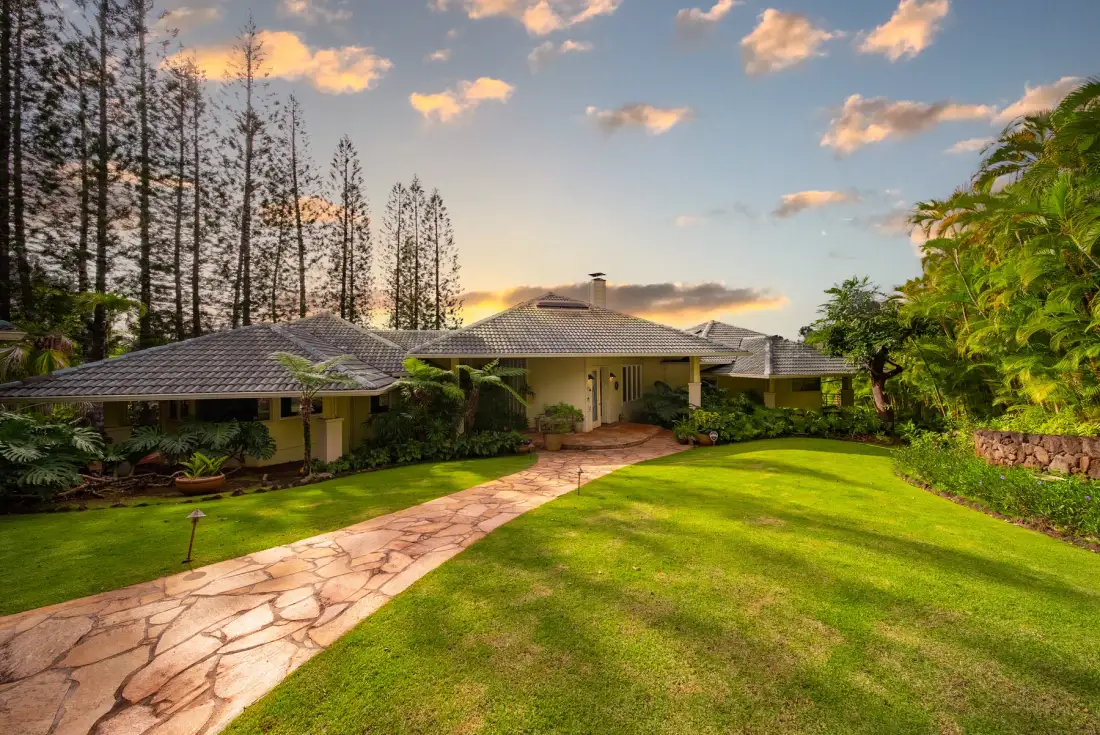 A single-story house sits beyond a stone path crossing a green lawn.
