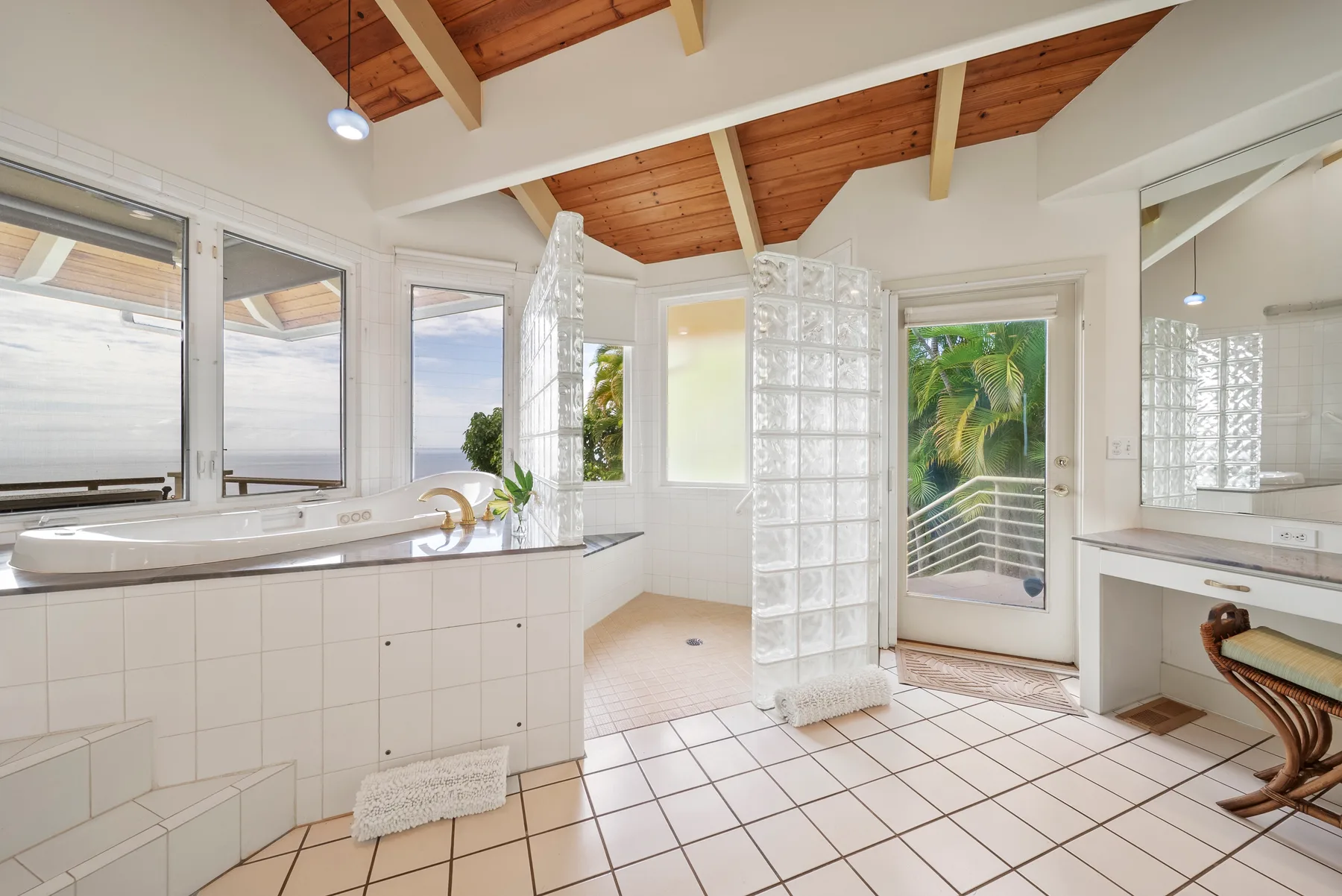 A bright bathroom with a tiled bathtub, glass-block partition, and large windows.