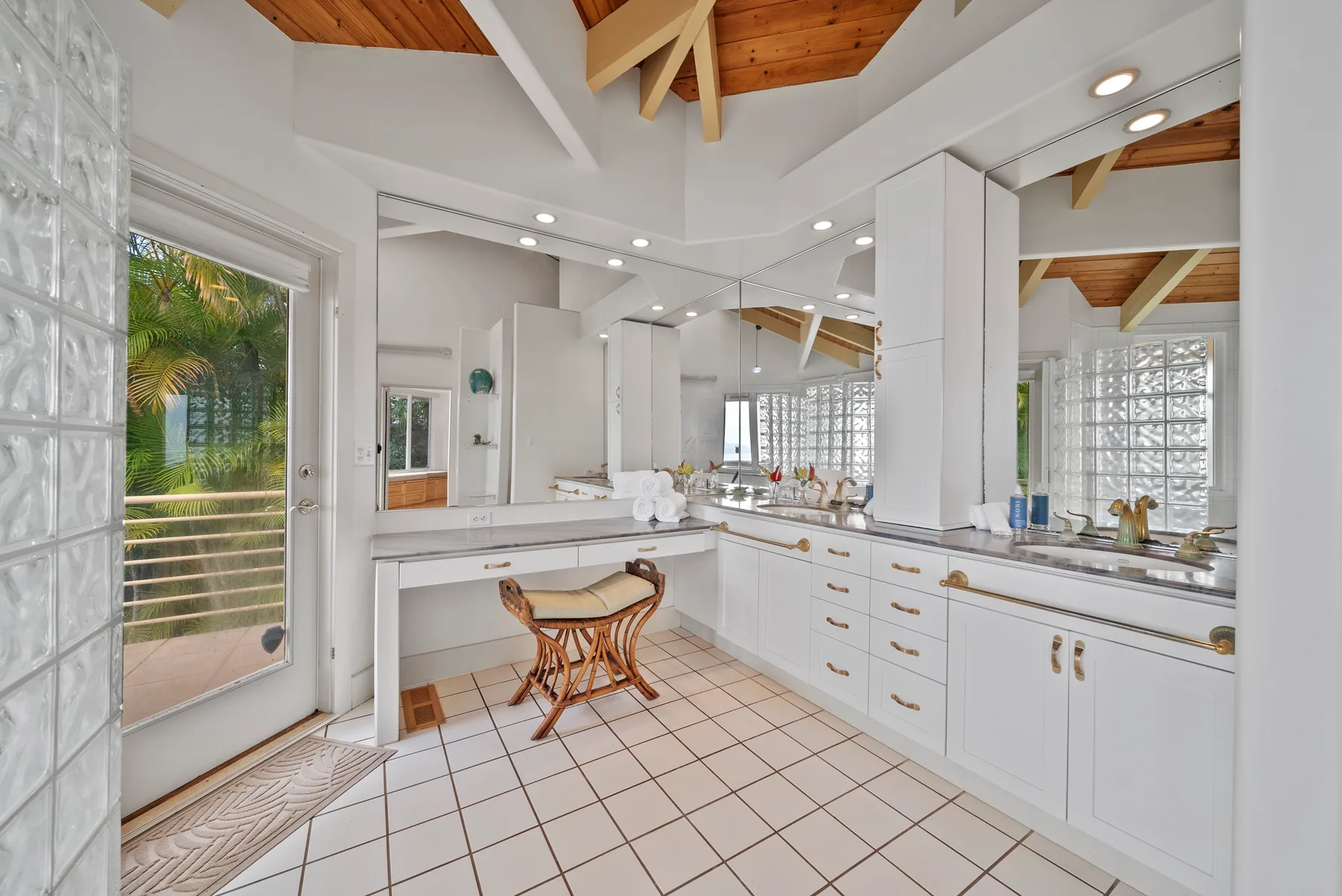 A bright kitchen with white cabinetry, tiled flooring, and a glass door opening onto greenery.