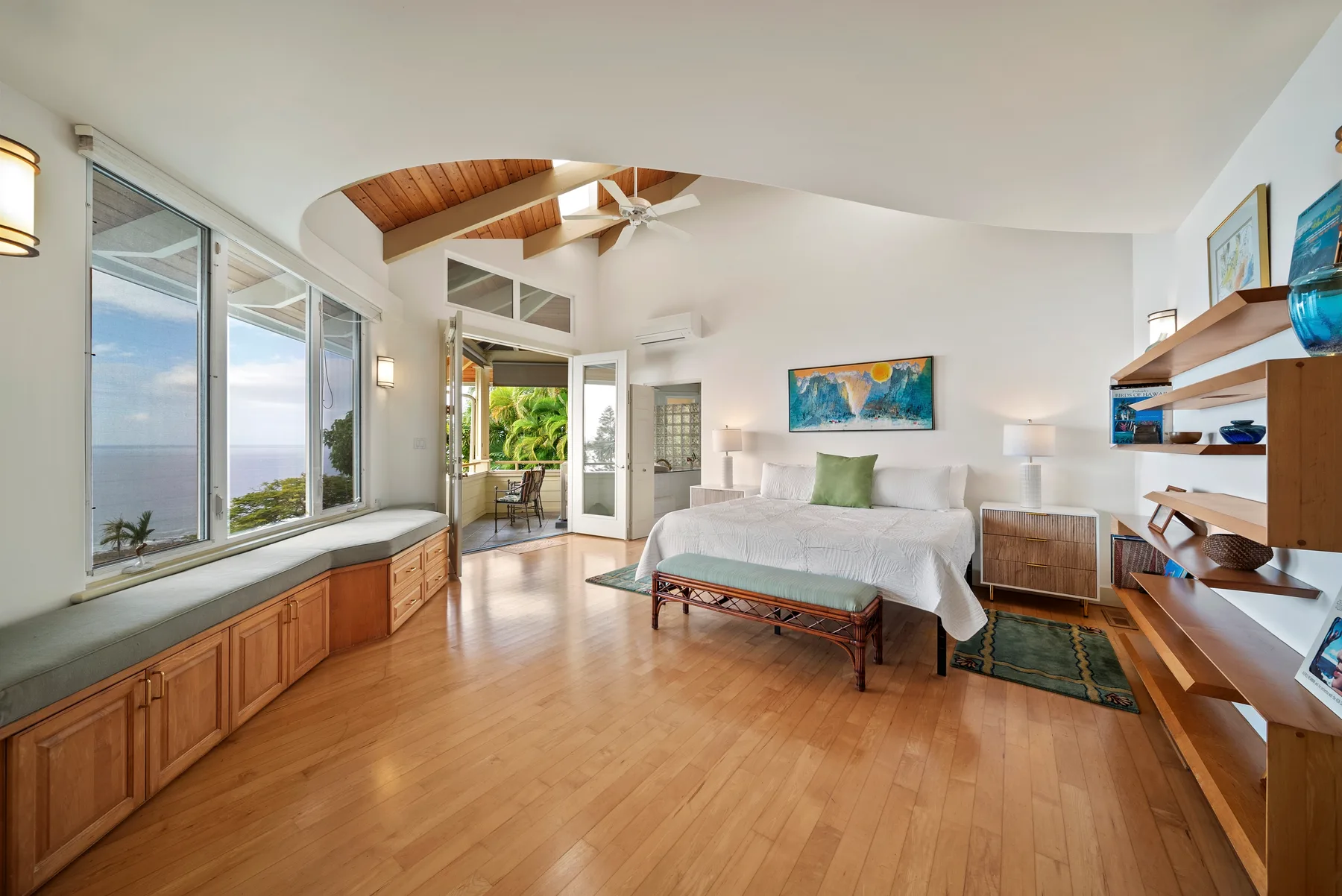 A bright bedroom with a bed, wood flooring, and large windows.