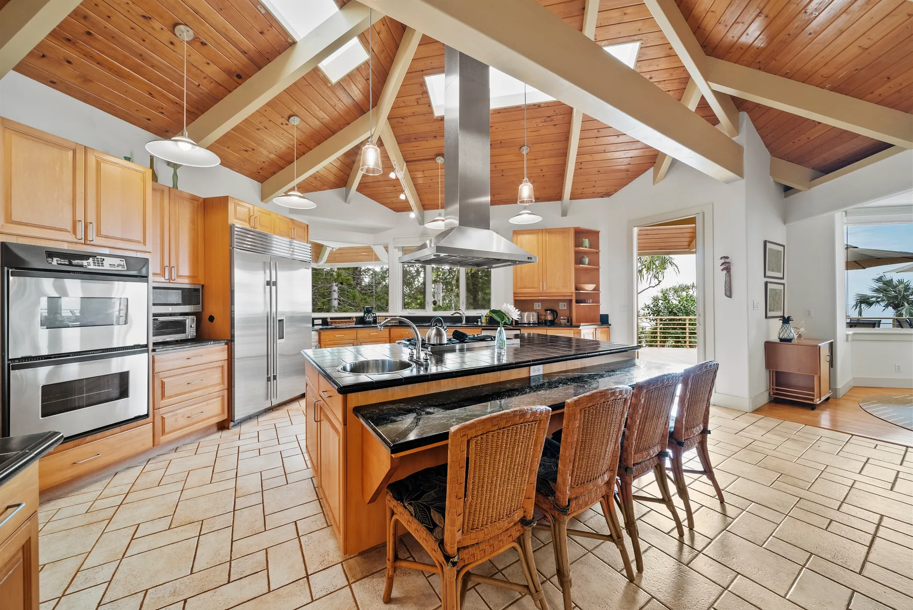 A spacious kitchen with a central island, wooden cabinetry, and a vaulted wood ceiling.