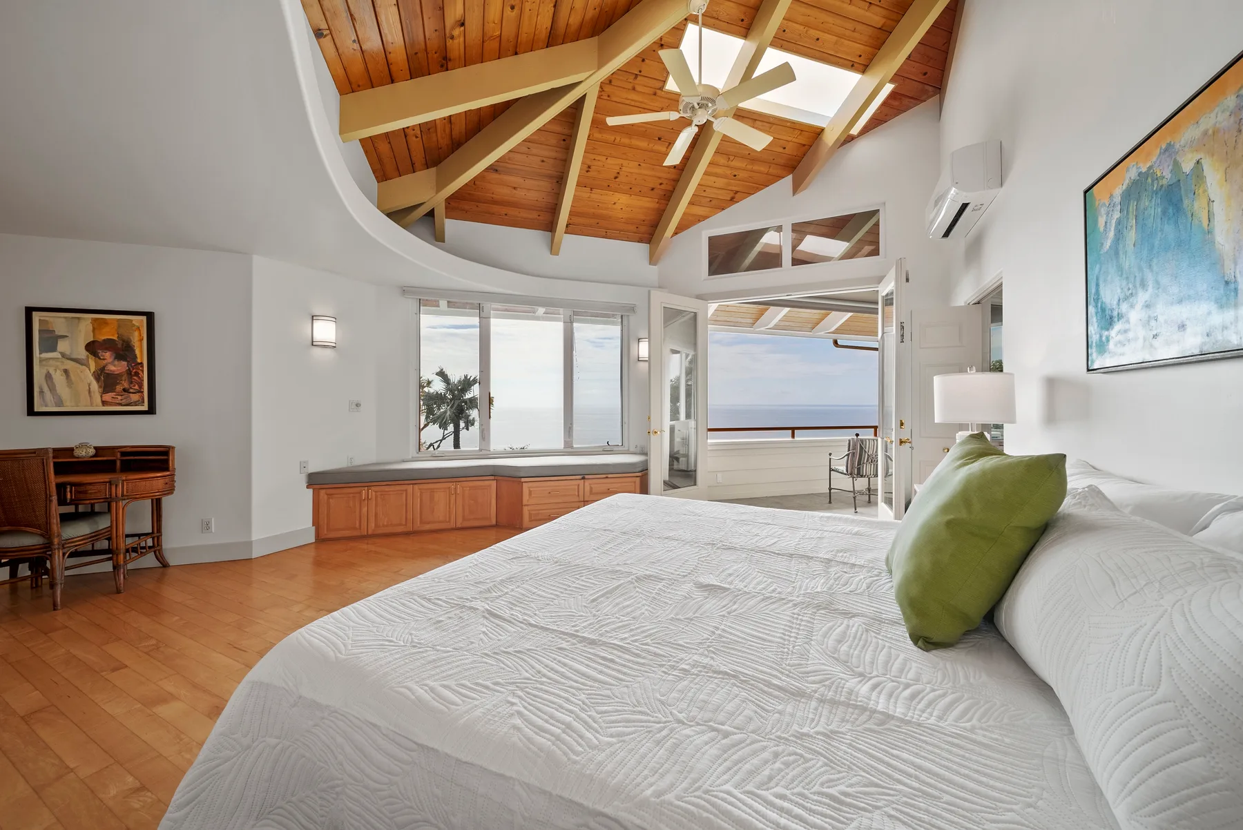 A bright bedroom with a large bed beneath a vaulted wooden ceiling.