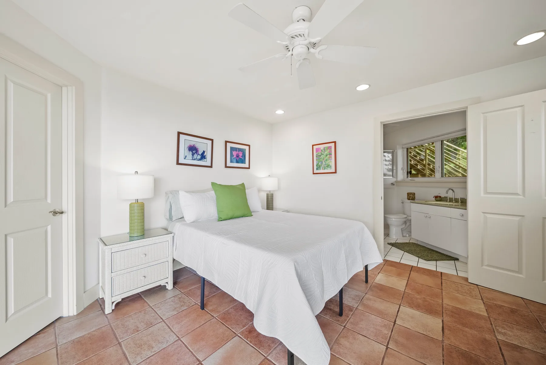 A bright bedroom with a white bed, green accent pillow, and tiled floor.