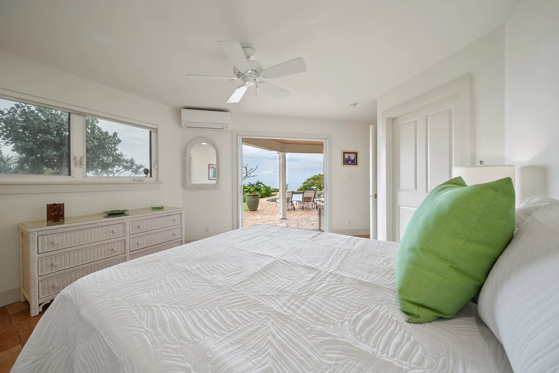 A bright bedroom with a white bed and green accent pillows.