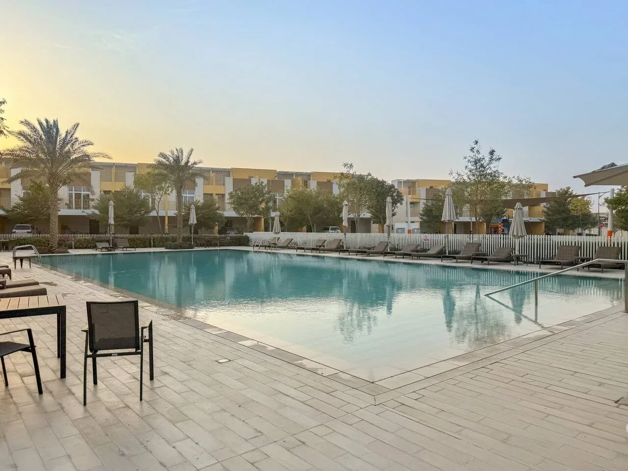 Una piscina está rodeada por una terraza pavimentada y asientos al aire libre.