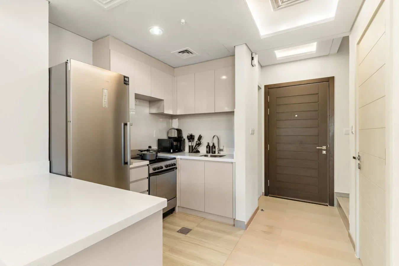 Una cocina luminosa con armarios blancos, electrodomésticos de acero inoxidable y una puerta de madera oscura.