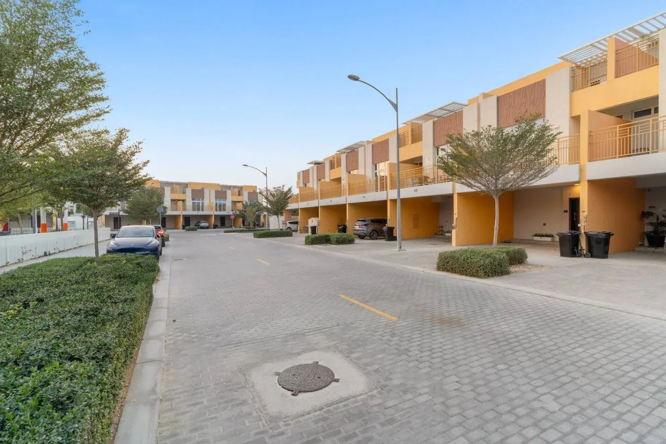 Una calle pavimentada pasa entre edificios modernos, con coches estacionados y árboles.
