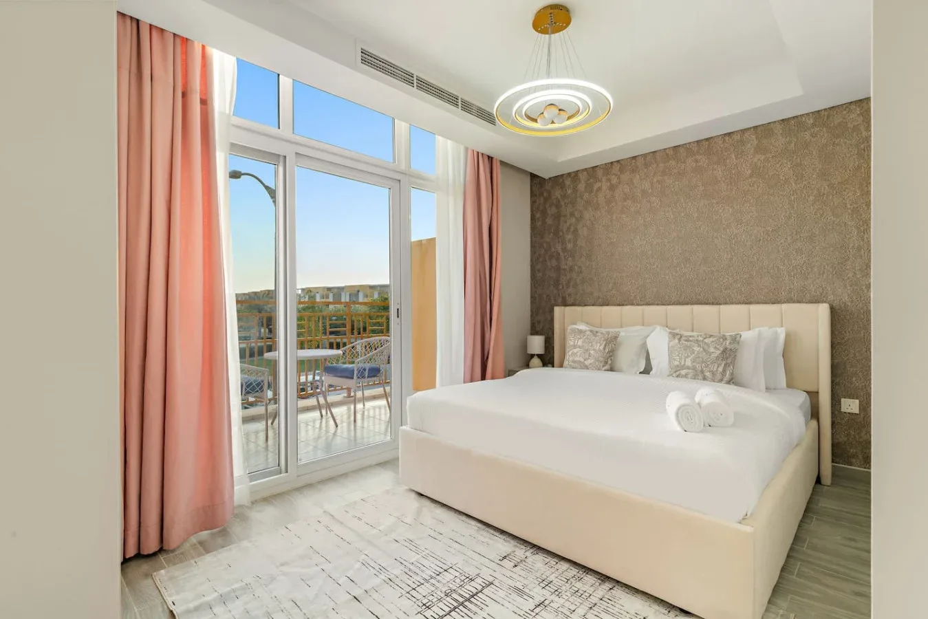 Un dormitorio luminoso con una cama grande junto a puertas de vidrio que dan a un balcón.