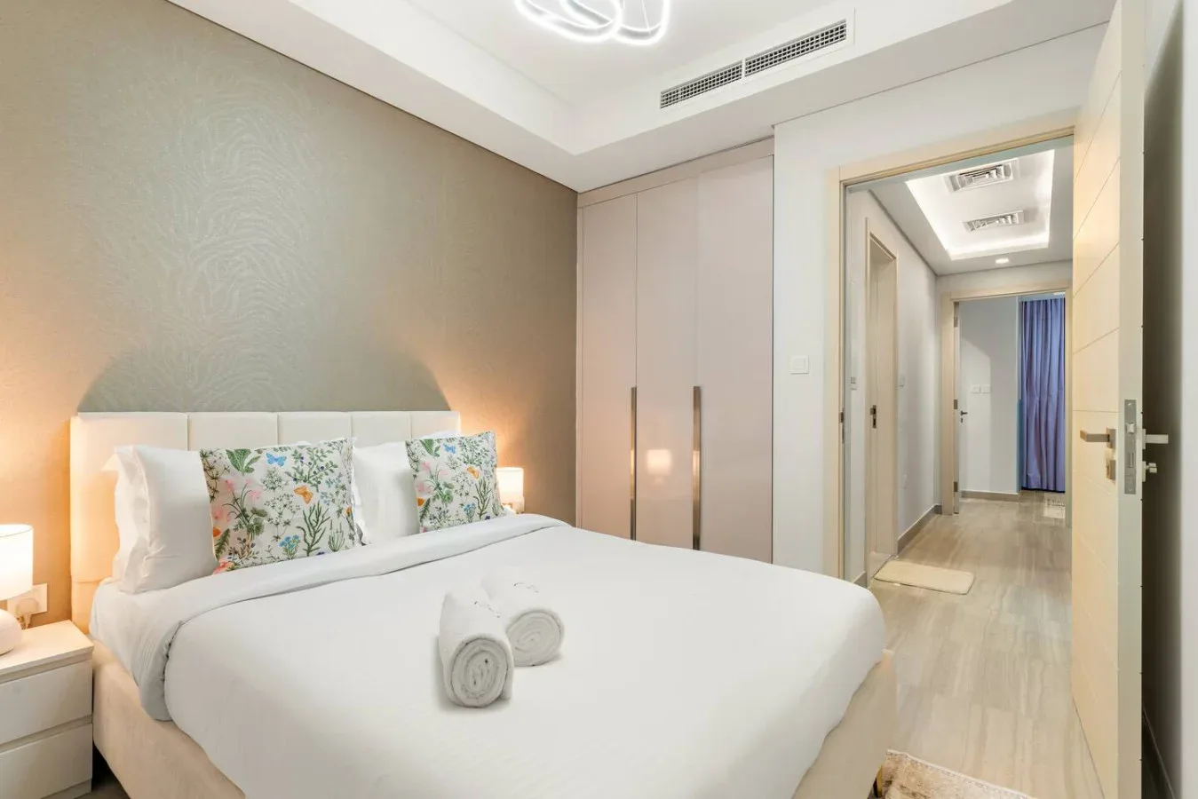 Un dormitorio luminoso con una cama bien tendida y un pasillo visible tras la puerta abierta.