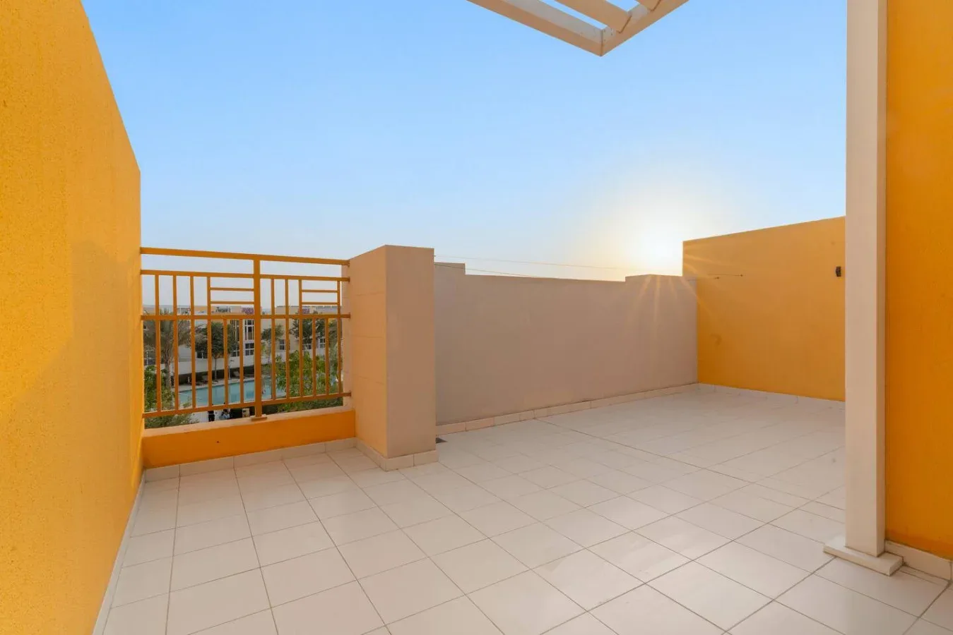 Una terraza soleada con suelo de baldosas y una barandilla metálica.