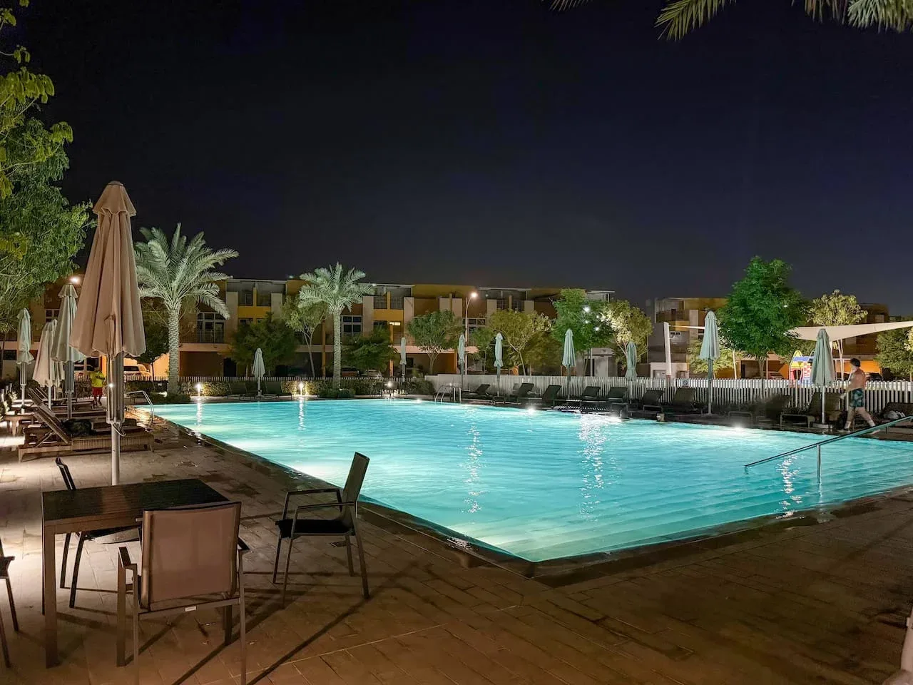 Una piscina exterior iluminada por la noche, con asientos alrededor.