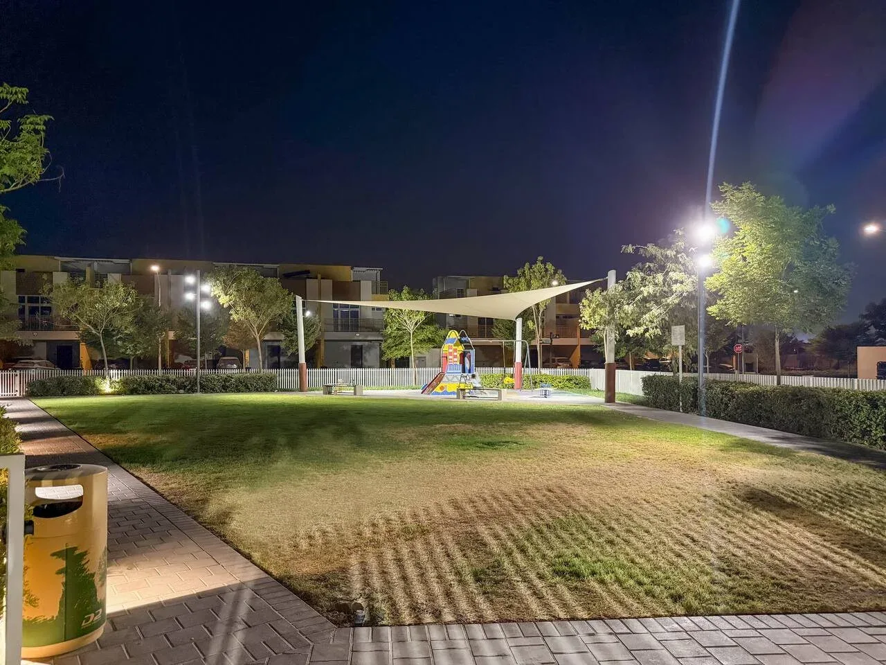 Una zona de juegos al aire libre ajardinada, con juegos coloridos bajo una cubierta por la noche.
