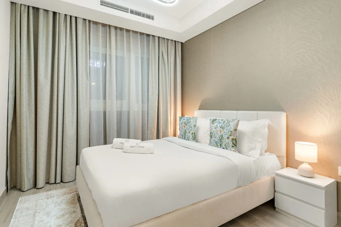 Un dormitorio con una cama bien tendida, una mesita de noche y cortinas largas.
