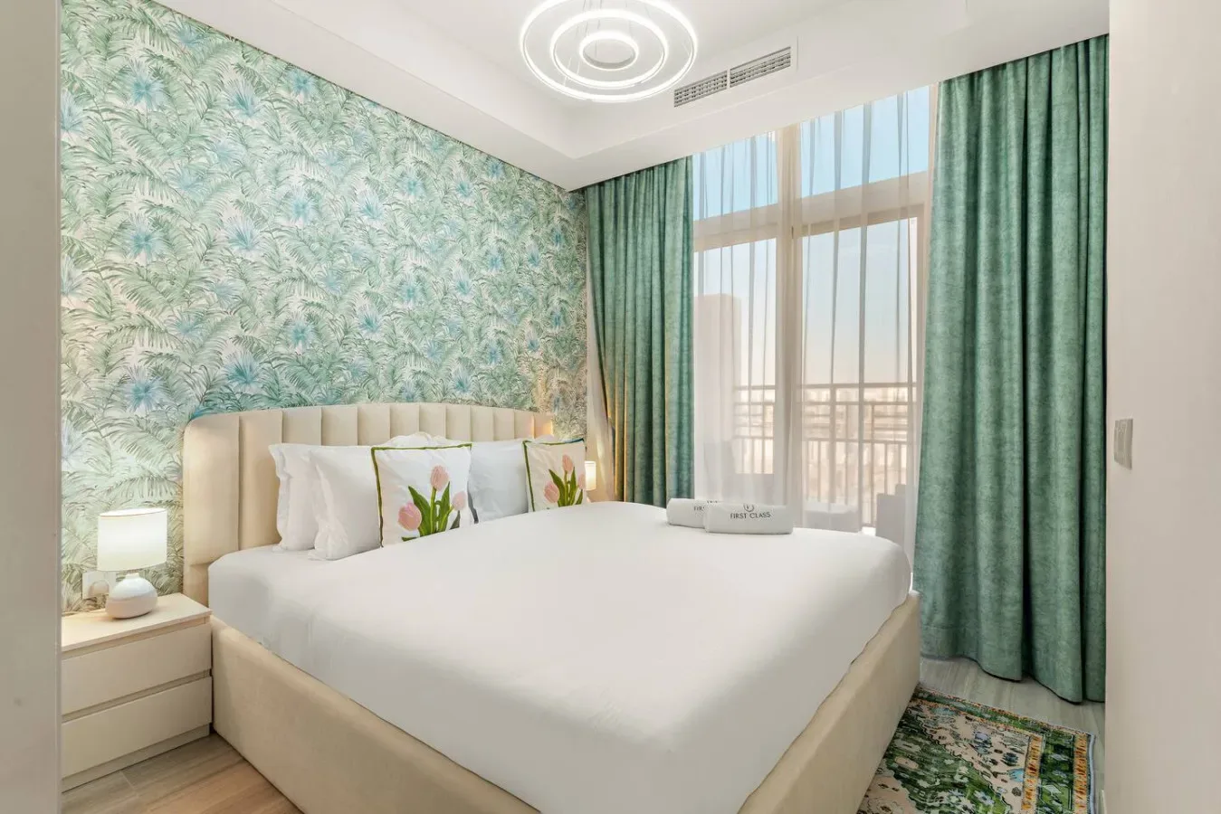Un dormitorio luminoso con una cama grande, papel tapiz de hojas y cortinas verdes.