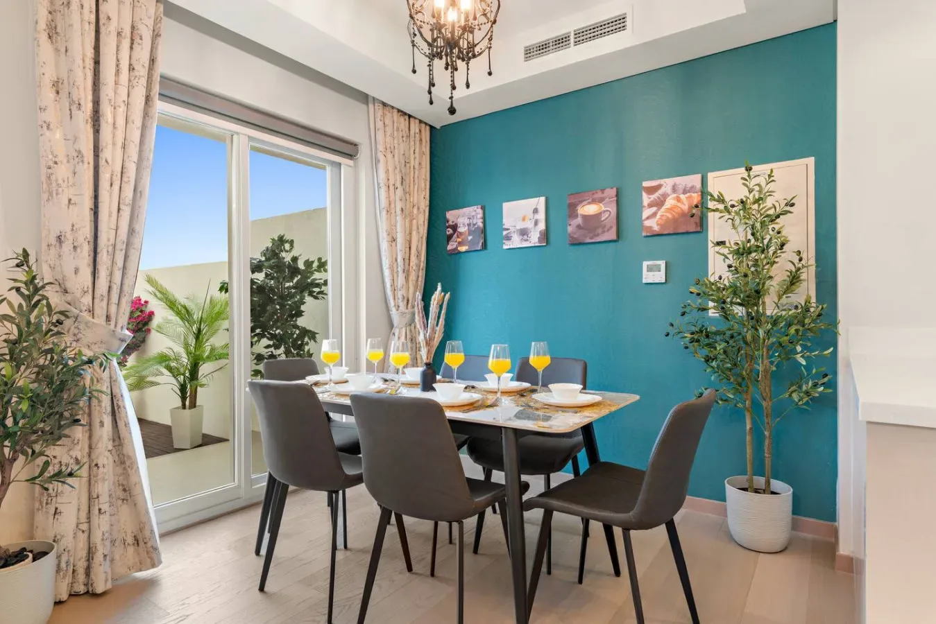 Comedor con una mesa puesta junto a grandes ventanales y una pared de acento turquesa.