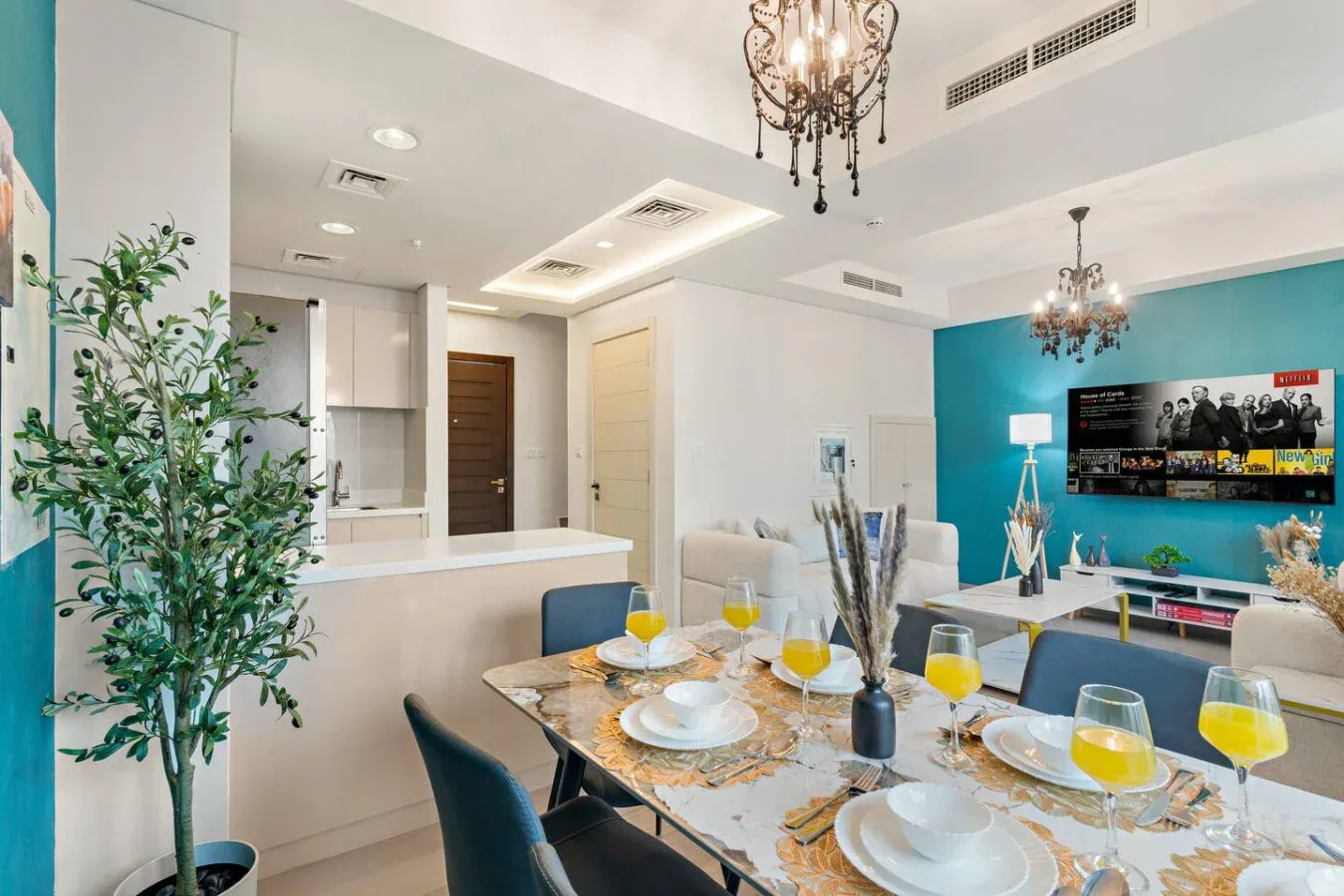Zona de comedor y estar con una mesa puesta y un televisor junto a una pared color turquesa.