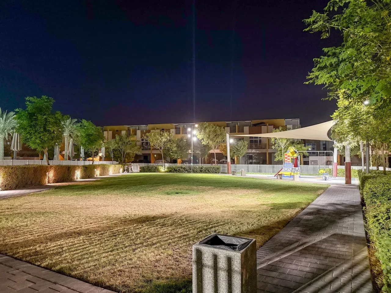 Un patio ajardinado de noche con césped, árboles y un sendero pavimentado.