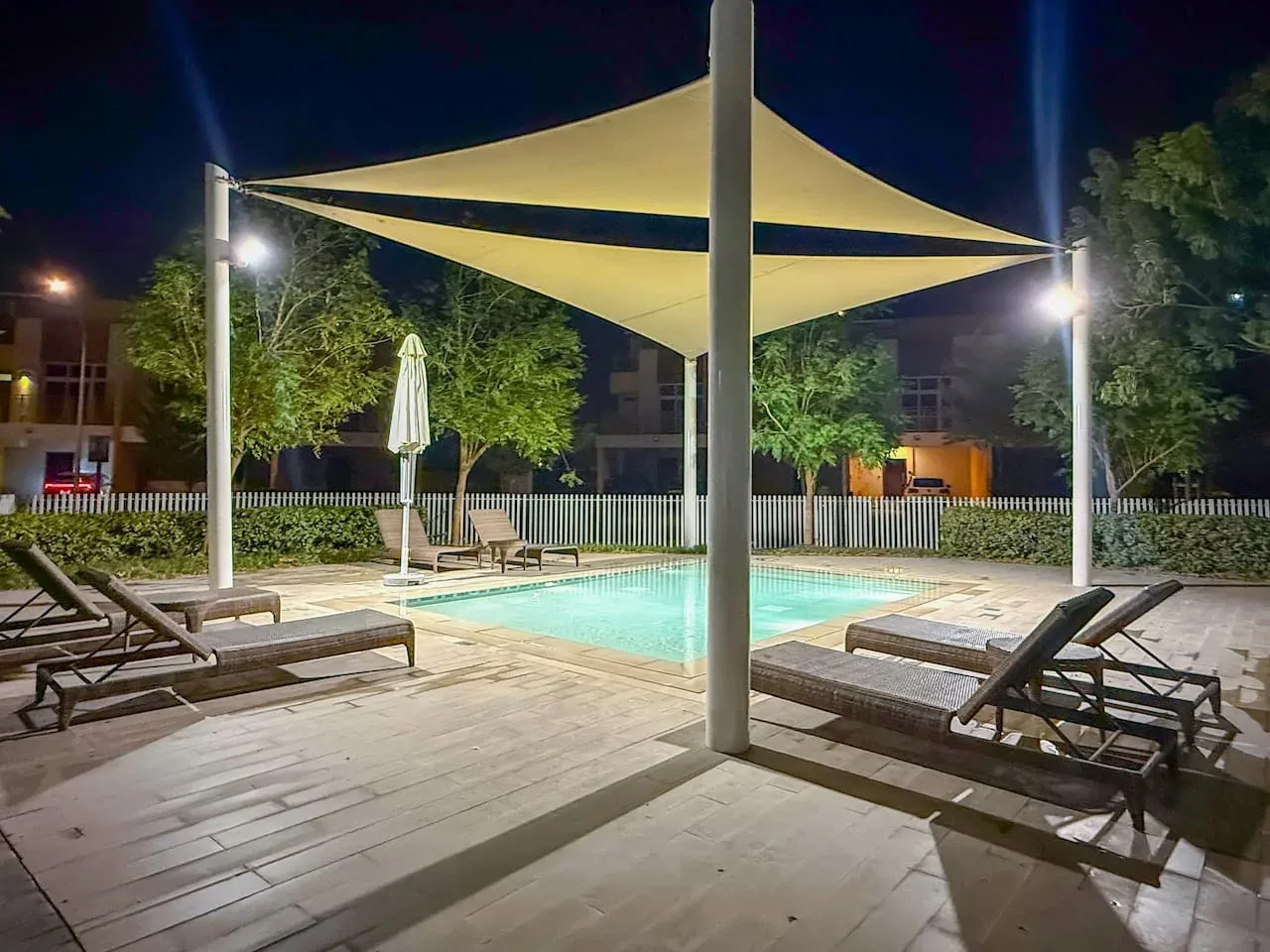 Una piscina exterior iluminada se encuentra bajo una gran cubierta de sombra por la noche.