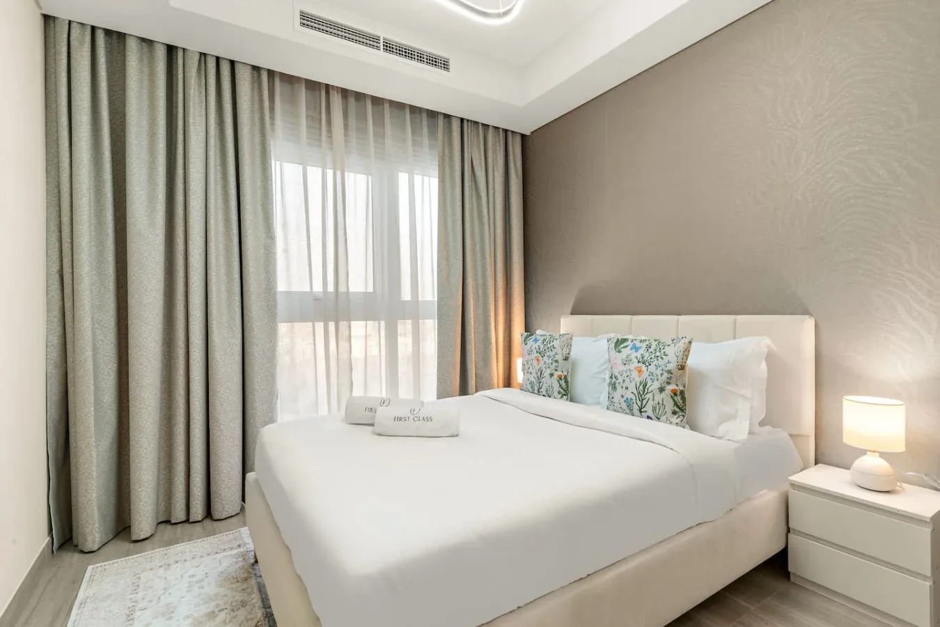 Un dormitorio con una cama bien tendida junto a una ventana con cortinas.