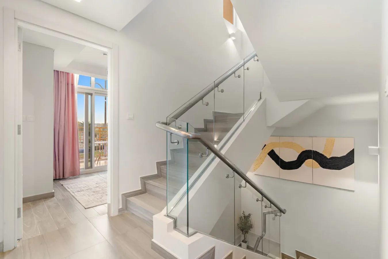 Una escalera luminosa con barandilla de vidrio y una pintura abstracta en la pared.