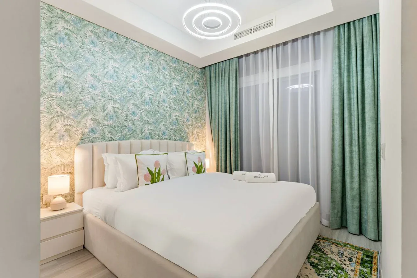 Un dormitorio con una cama grande, papel pintado estampado y cortinas verdes.
