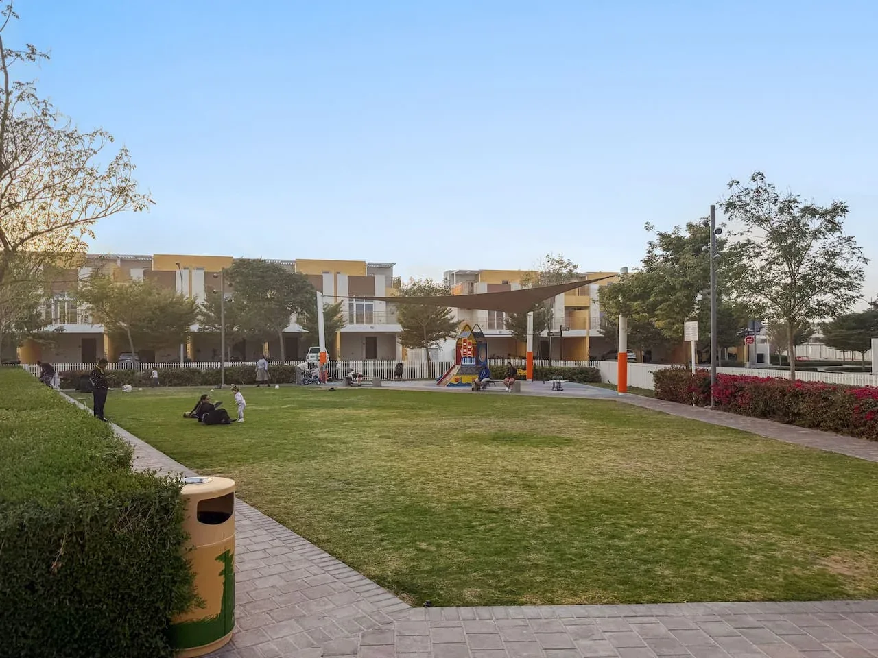 Un patio ajardinado con césped amplio, senderos pavimentados y un pequeño parque infantil.