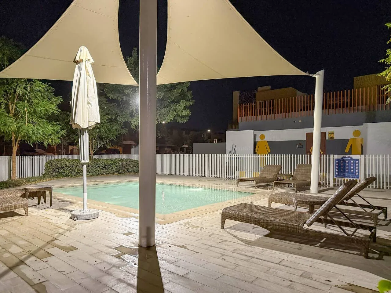 Una piscina bajo una gran cubierta de sombra, con tumbonas en la zona pavimentada.