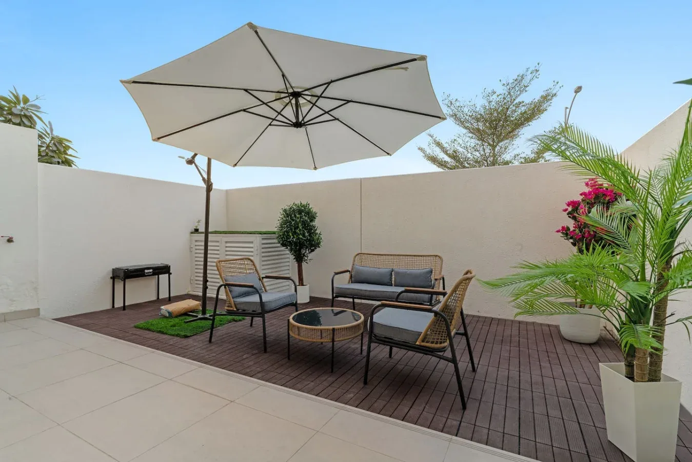 Un patio exterior con asientos bajo una gran sombrilla y plantas en macetas.
