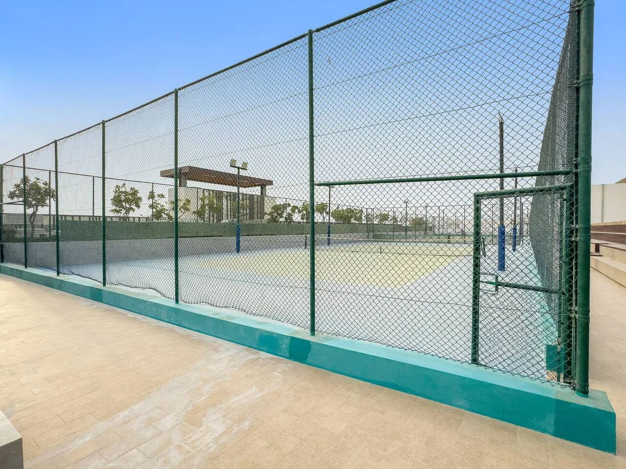 Una cancha deportiva al aire libre cercada, con un camino pavimentado al lado.