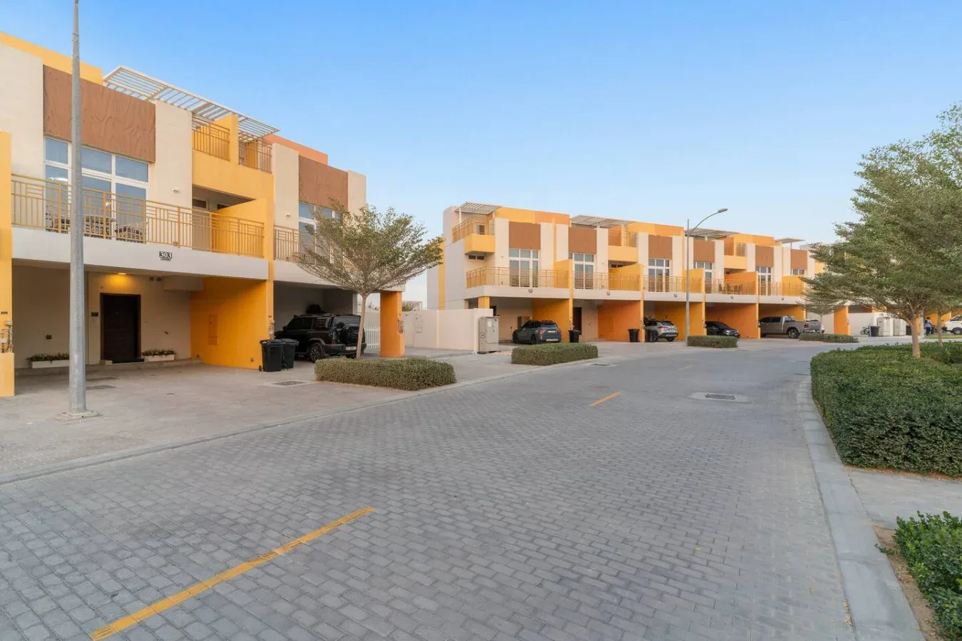 Una calle pavimentada pasa junto a una fila de edificios modernos con vehículos estacionados.