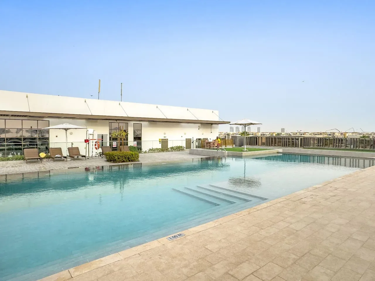 Una piscina al aire libre junto a un edificio blanco bajo y una terraza pavimentada.