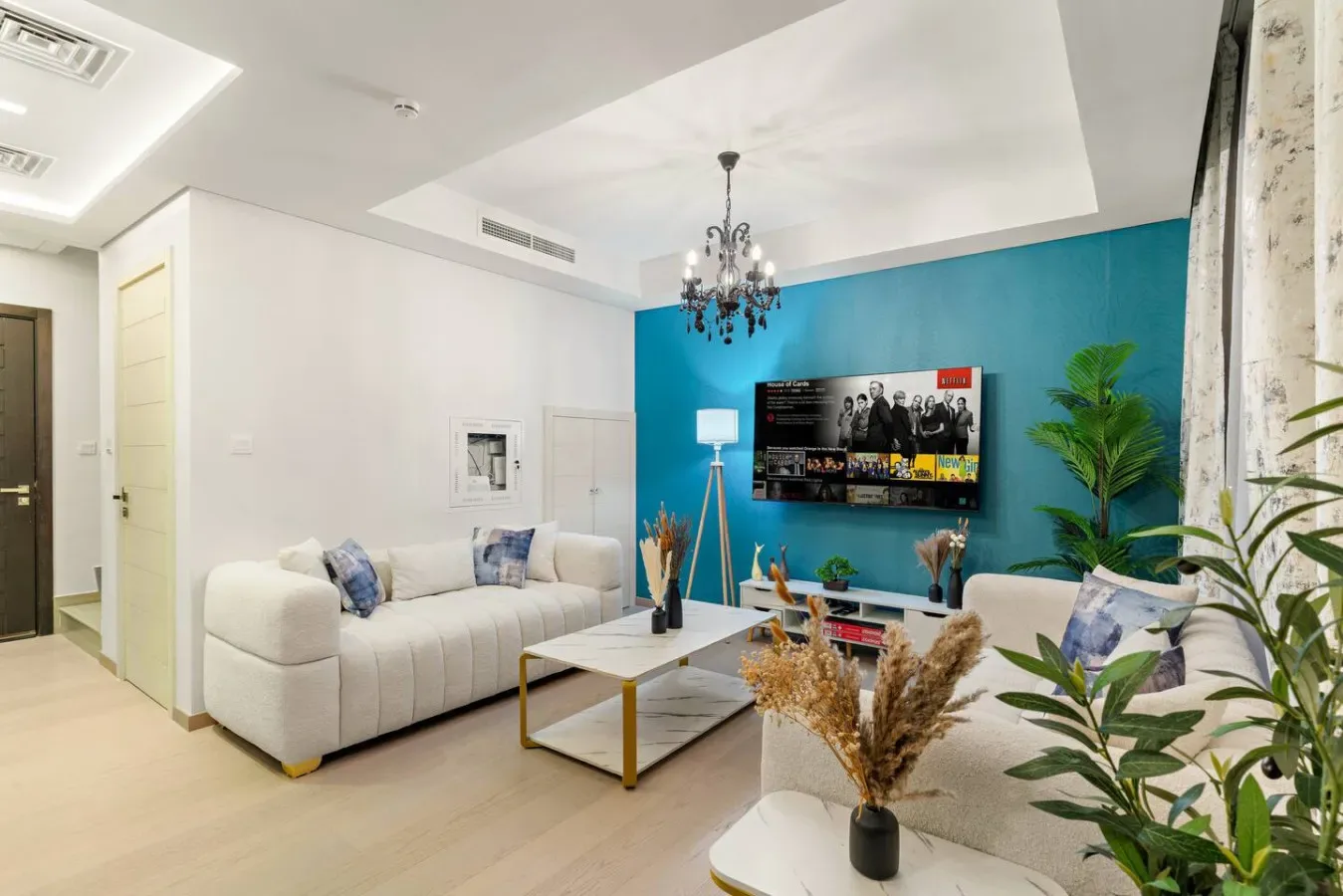 Una sala luminosa con un sofá seccional blanco frente a un televisor en una pared azul.
