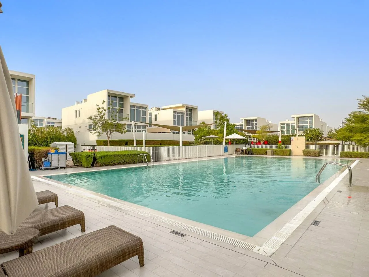 Una piscina al aire libre junto a edificios residenciales modernos, con asientos en la terraza.