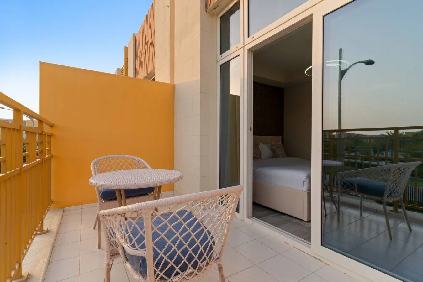 Una terraza con suelo de baldosas, asientos tejidos y una puerta abierta a un dormitorio.