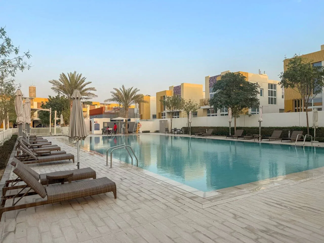 Una piscina al aire libre está rodeada de asientos y edificios bajos.