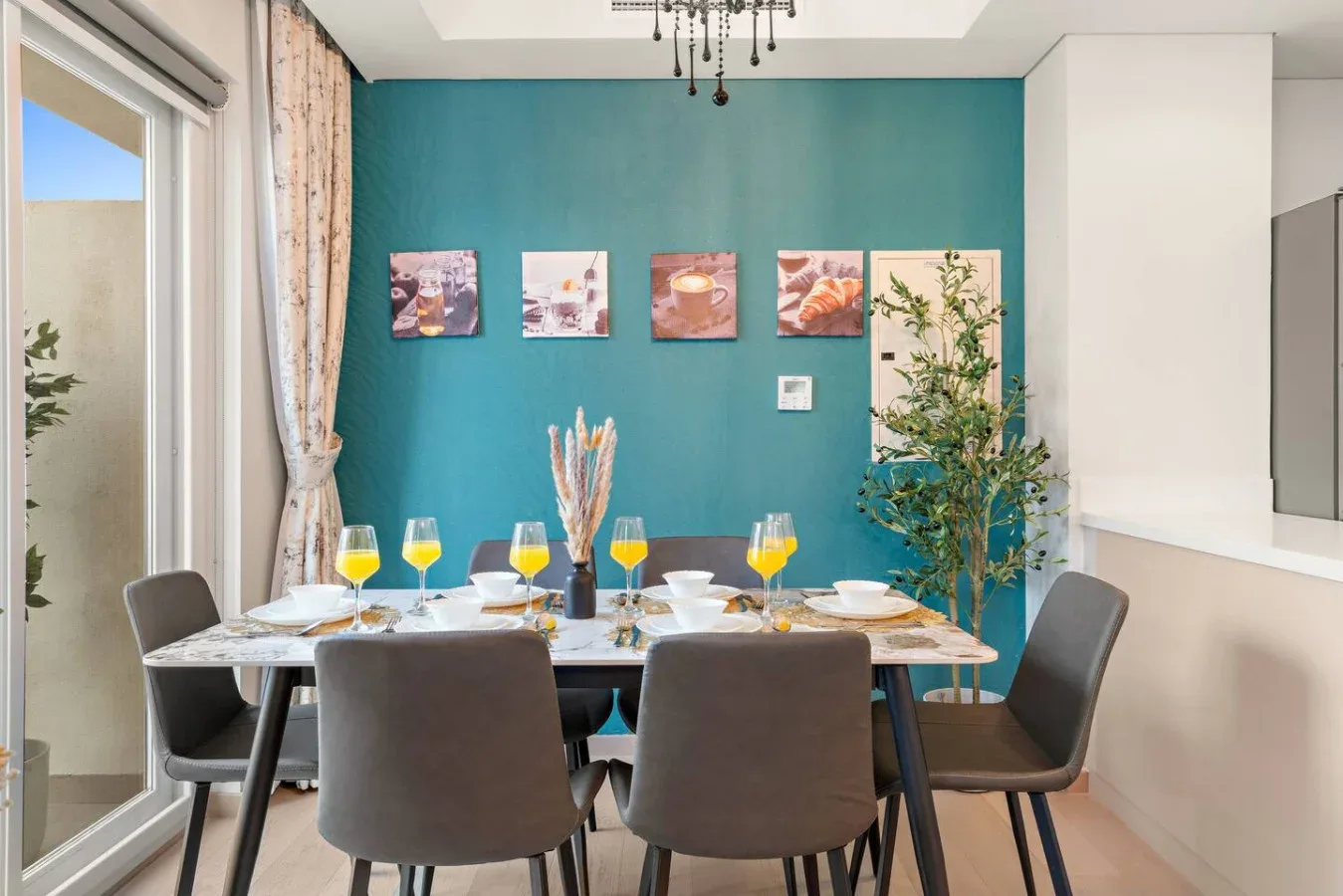 Un comedor con la mesa puesta, bebidas de colores y cuadros en una pared turquesa.