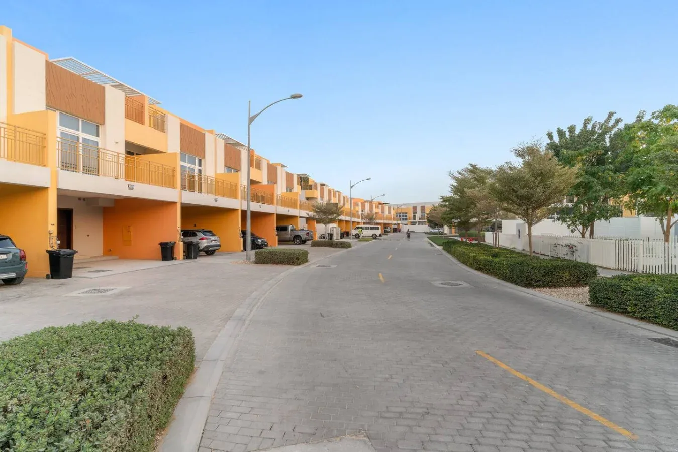 Una calle residencial pavimentada pasa junto a casas adosadas con balcones y autos estacionados.