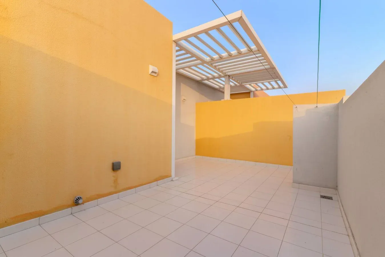 Un patio exterior embaldosado con paredes amarillas y una pérgola de listones.