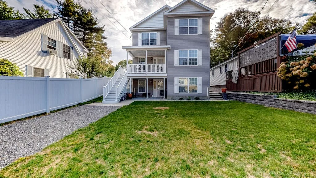 A gray multi-story house stands behind a grassy backyard and gravel path.