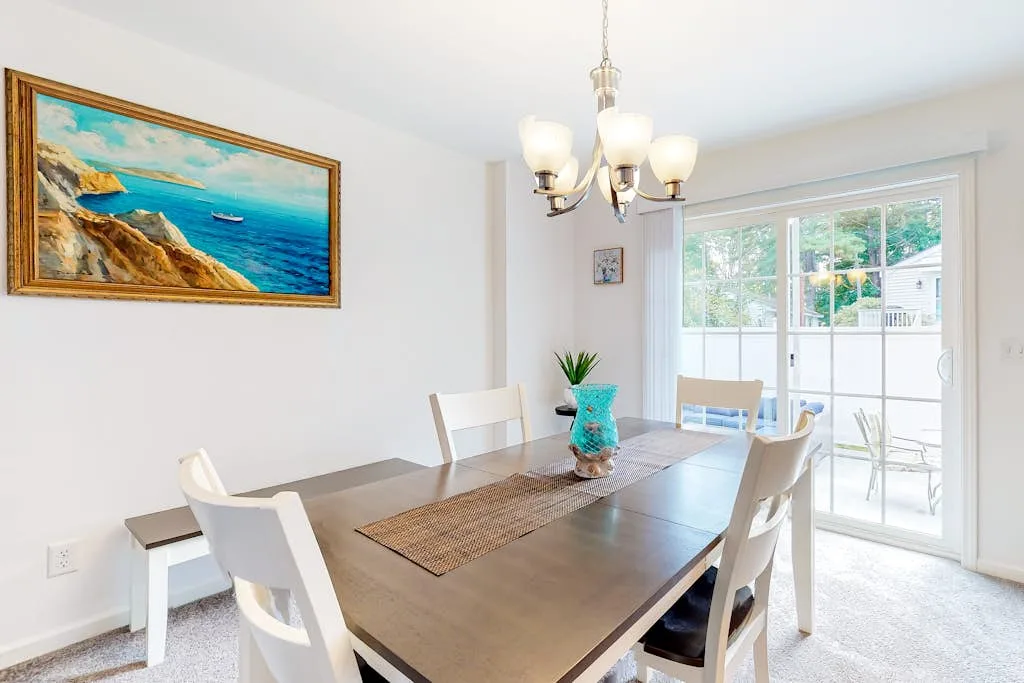A dining area with a large table, seating, and a chandelier beside glass doors.