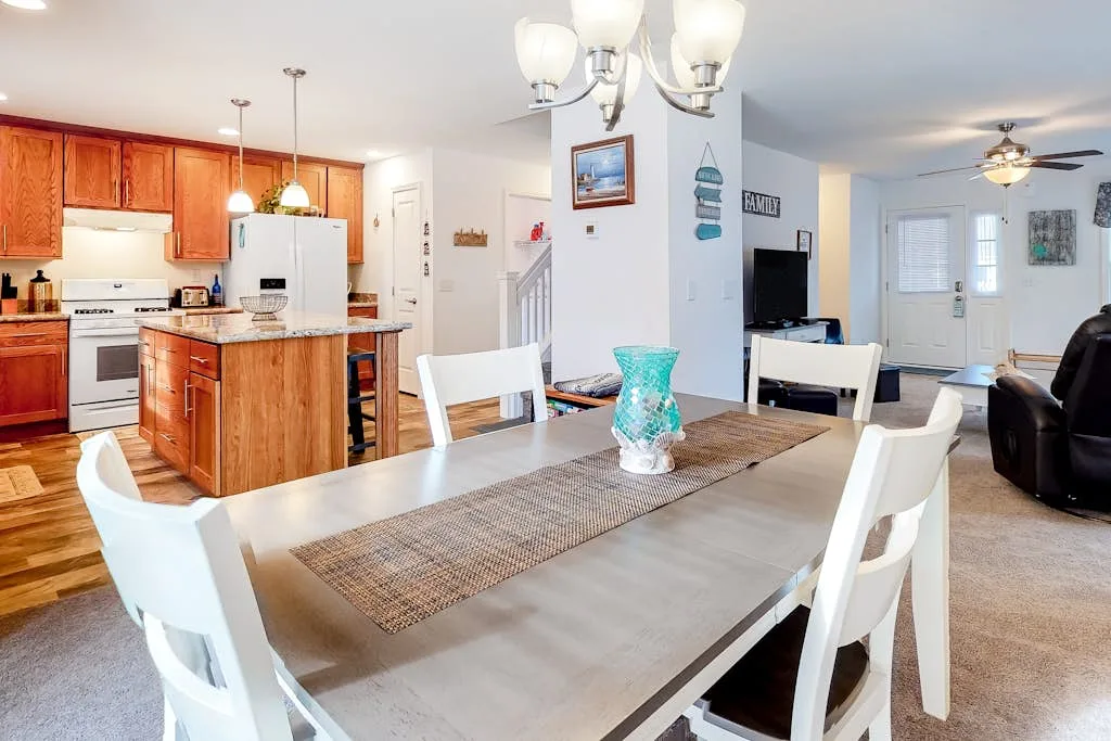 An open-plan dining and kitchen area with a long table and wooden cabinets.