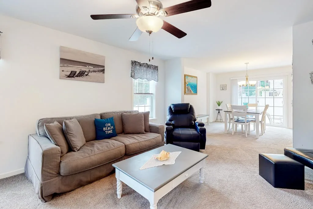 A living room with a sofa, armchair, and coffee table beside a dining area.