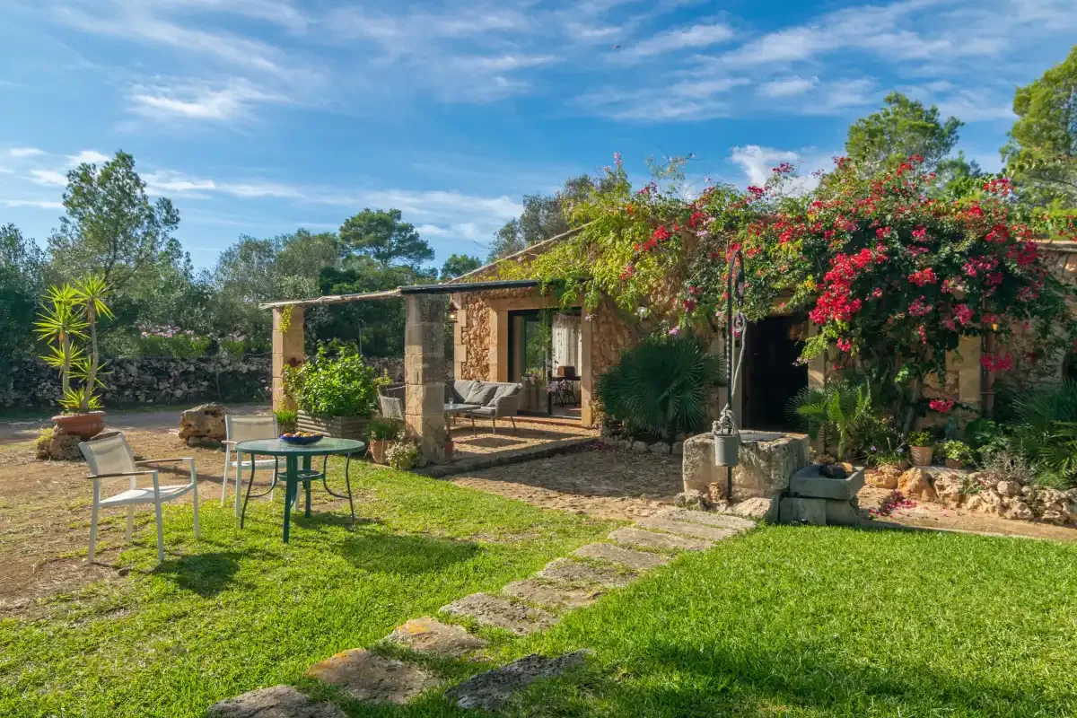 Un patio ajardinado con asientos al aire libre junto a una casa de piedra cubierta de flores.