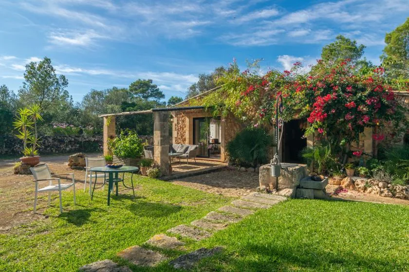 Una casa de piedra da a un patio ajardinado con asientos al aire libre y enredaderas en flor.