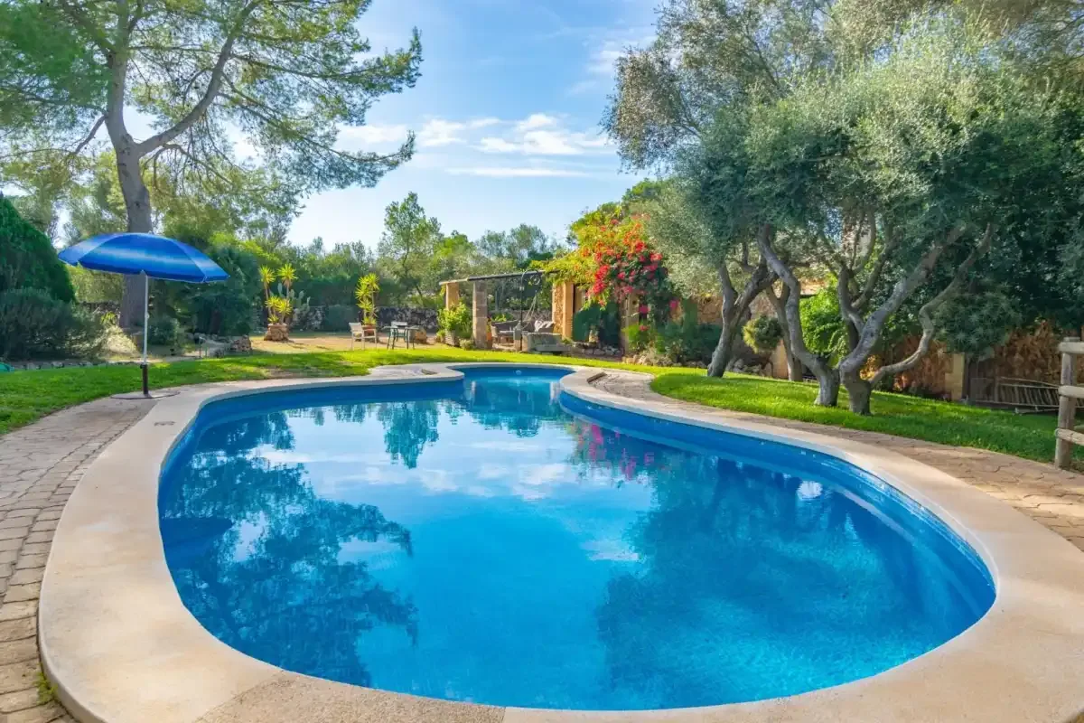 Una piscina exterior curva está rodeada de árboles y senderos ajardinados.