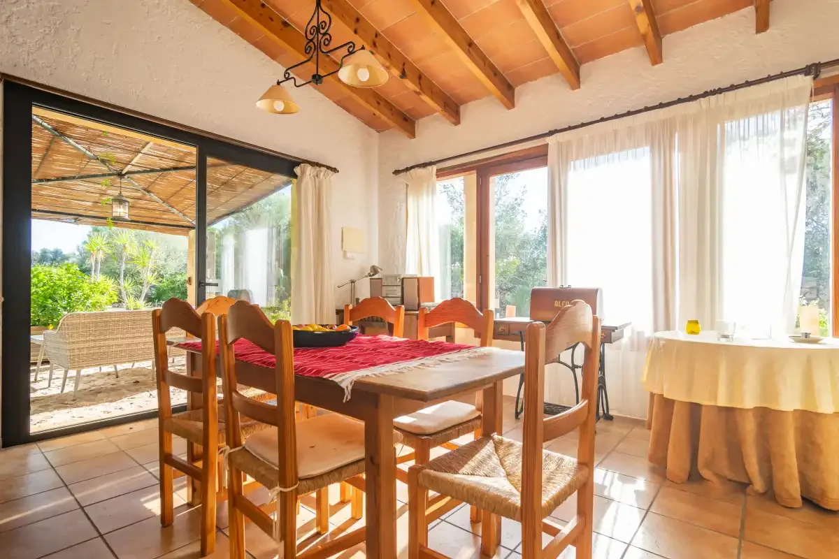 Un comedor luminoso con una mesa de madera junto a grandes ventanales y una puerta al patio.