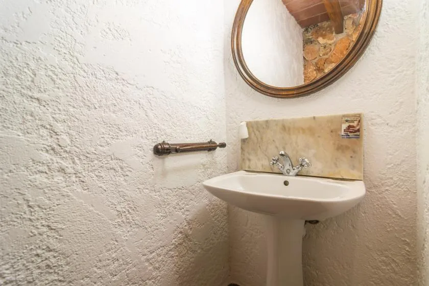 Un lavabo de baño está frente a paredes texturizadas, bajo un espejo redondo.