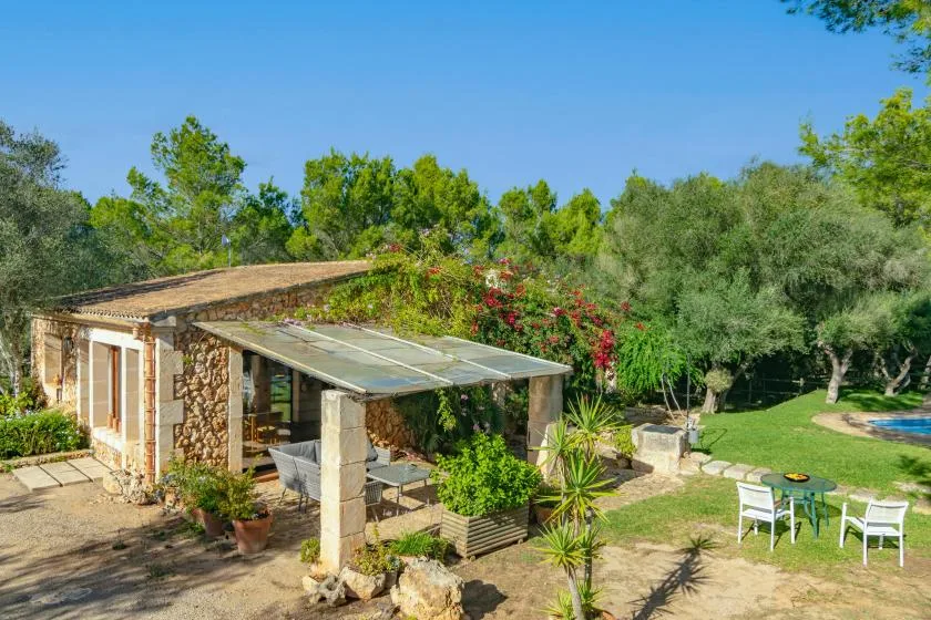 Una casa de piedra con patio cubierto da a un jardín con asientos al aire libre.